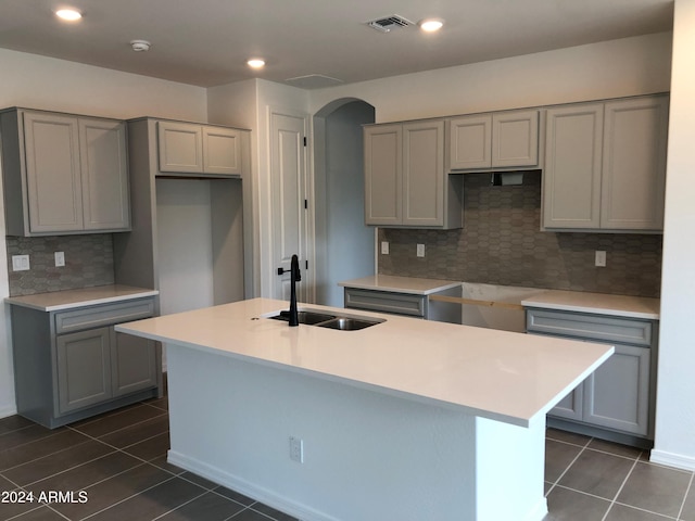 kitchen featuring decorative backsplash, a kitchen island with sink, gray cabinetry, sink, and dark tile patterned flooring