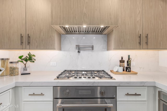 kitchen featuring decorative backsplash, wall chimney range hood, white cabinets, light brown cabinetry, and appliances with stainless steel finishes