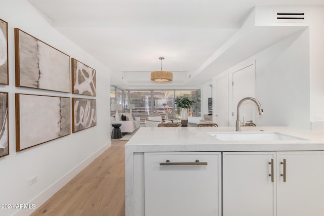 kitchen with sink, kitchen peninsula, light hardwood / wood-style floors, decorative light fixtures, and white cabinets