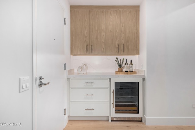 bar featuring decorative backsplash, wine cooler, light brown cabinetry, and light wood-type flooring