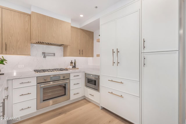 kitchen featuring appliances with stainless steel finishes, backsplash, light hardwood / wood-style floors, white cabinets, and light brown cabinets