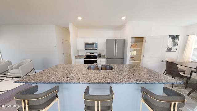 kitchen featuring white cabinetry, sink, light stone counters, a center island with sink, and appliances with stainless steel finishes