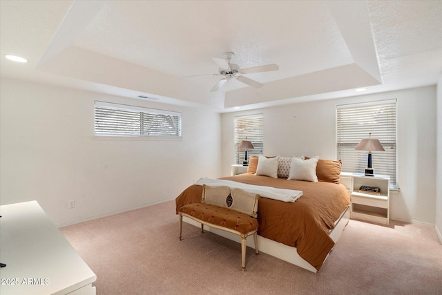 bedroom with light carpet, a textured ceiling, a raised ceiling, and ceiling fan