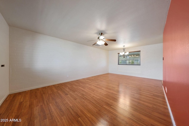 empty room featuring brick wall, baseboards, wood finished floors, and ceiling fan with notable chandelier