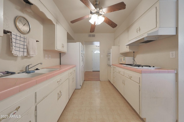 kitchen featuring white appliances, tile counters, white cabinets, and light floors