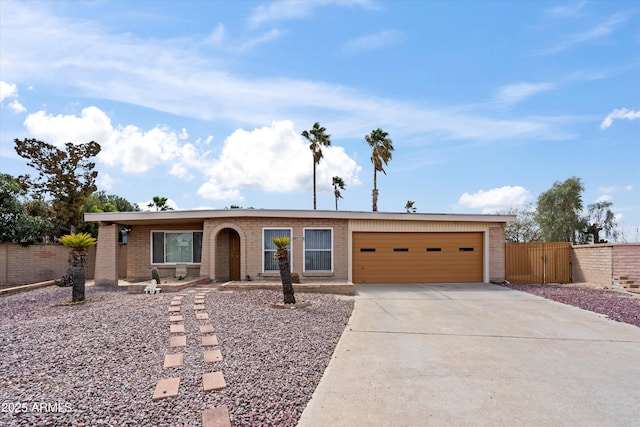 ranch-style home featuring brick siding, fence, a garage, driveway, and a gate