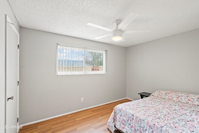 bedroom with a ceiling fan, wood finished floors, baseboards, and a textured ceiling