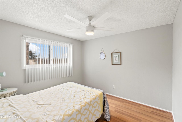 bedroom with ceiling fan, a textured ceiling, baseboards, and wood finished floors