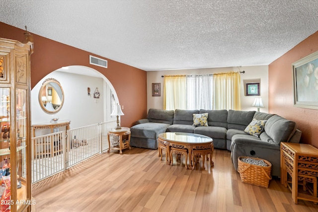 living room with light wood finished floors, visible vents, arched walkways, and a textured ceiling