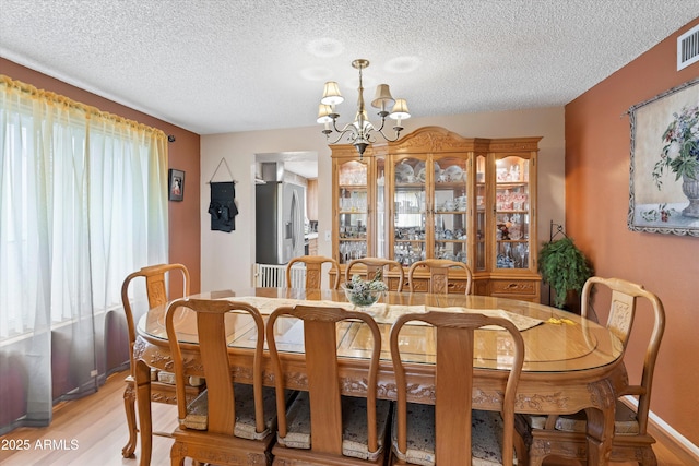 dining space with light wood-style flooring, a healthy amount of sunlight, visible vents, and a chandelier