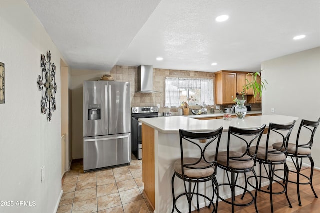 kitchen featuring a breakfast bar, backsplash, stainless steel appliances, wall chimney exhaust hood, and light countertops