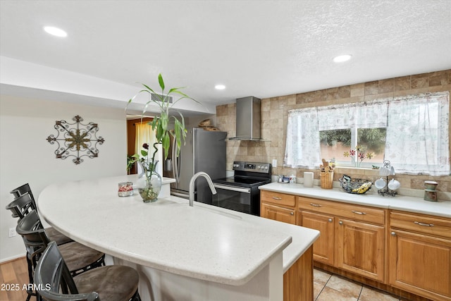 kitchen featuring a sink, tasteful backsplash, stainless steel appliances, a breakfast bar area, and wall chimney exhaust hood