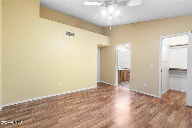 unfurnished bedroom featuring visible vents, baseboards, a spacious closet, light wood-style floors, and ensuite bathroom