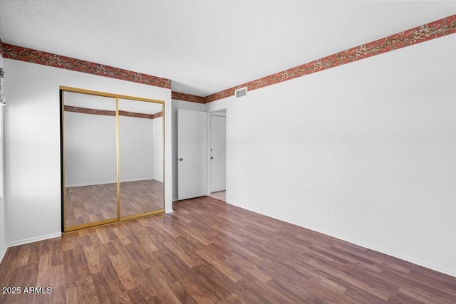 unfurnished bedroom featuring baseboards, visible vents, wood finished floors, and a closet