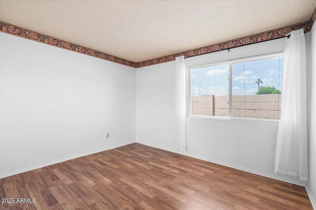 unfurnished room with baseboards, a textured ceiling, and wood finished floors
