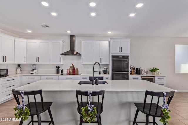 kitchen featuring a center island with sink, white cabinetry, wall chimney exhaust hood, and sink