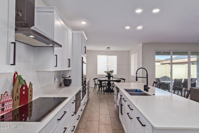 kitchen featuring a center island with sink, wall chimney exhaust hood, white cabinets, and sink