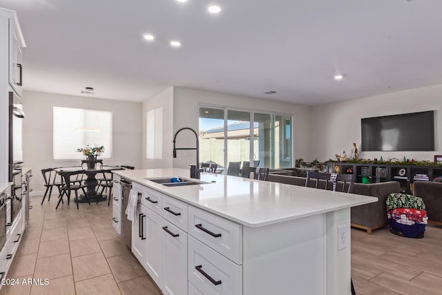 kitchen with a center island with sink, wall oven, white cabinetry, and sink