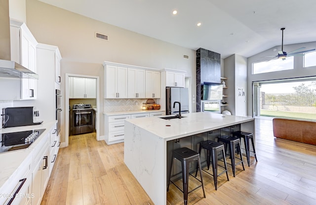 kitchen featuring wall chimney range hood, visible vents, a center island with sink, and white cabinetry