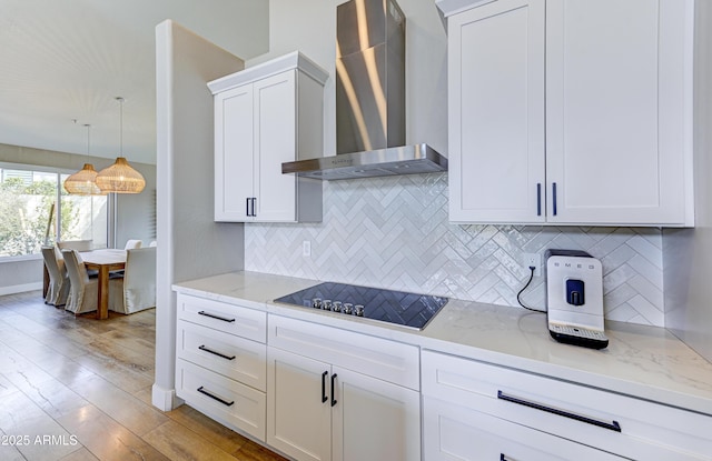 kitchen featuring wall chimney range hood, black electric stovetop, pendant lighting, and light stone counters