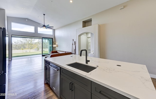 kitchen with light stone counters, a sink, vaulted ceiling, open floor plan, and dishwasher