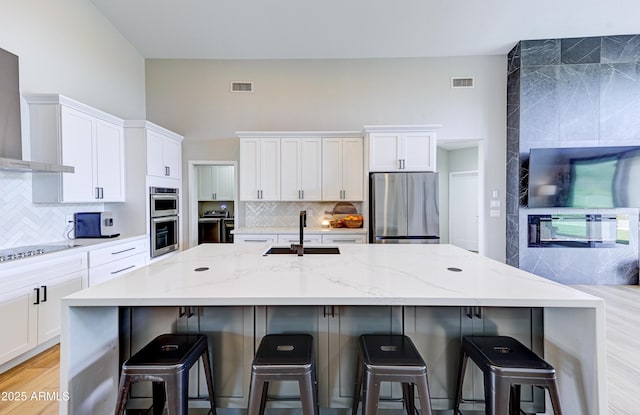 kitchen with stainless steel appliances, a spacious island, visible vents, wall chimney range hood, and a kitchen bar