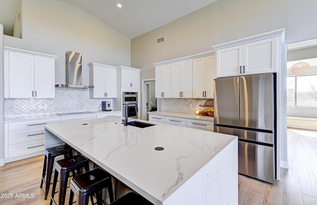 kitchen featuring appliances with stainless steel finishes, white cabinetry, a center island with sink, and wall chimney exhaust hood