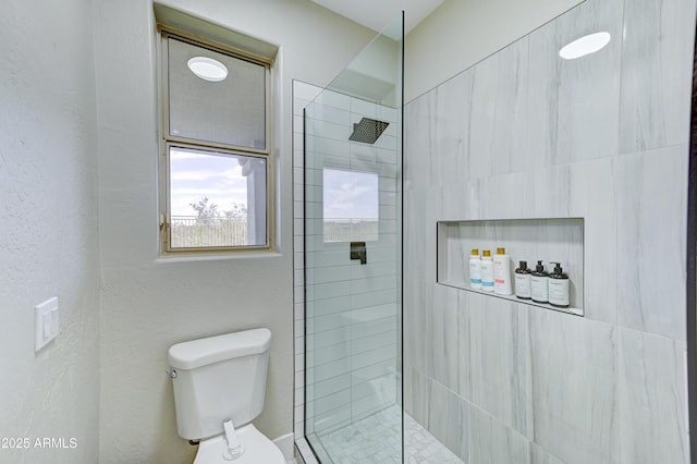 bathroom with tiled shower, a textured wall, and toilet