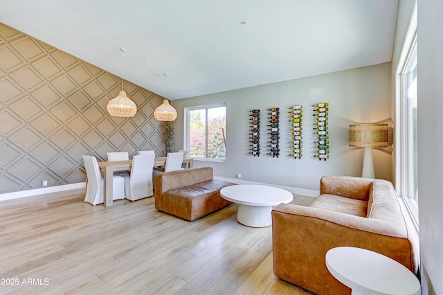 living area featuring wallpapered walls, an accent wall, baseboards, and light wood finished floors