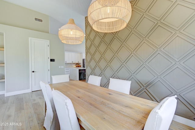 dining room with an accent wall, light wood-type flooring, visible vents, and baseboards