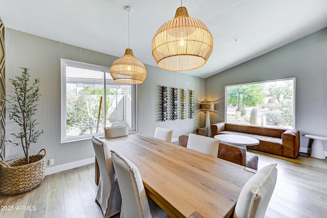 dining area with light wood-style floors, baseboards, vaulted ceiling, and a textured wall