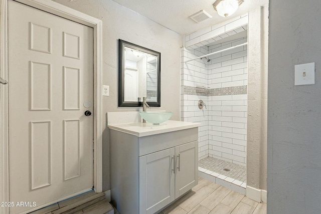 bathroom with a textured ceiling, tiled shower, and vanity