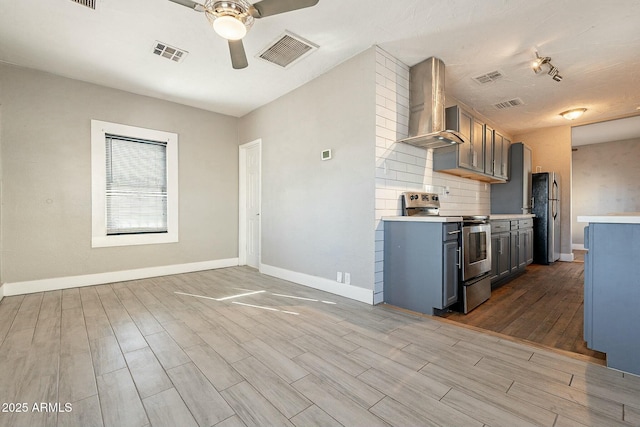 kitchen with tasteful backsplash, ceiling fan, wall chimney range hood, appliances with stainless steel finishes, and gray cabinetry