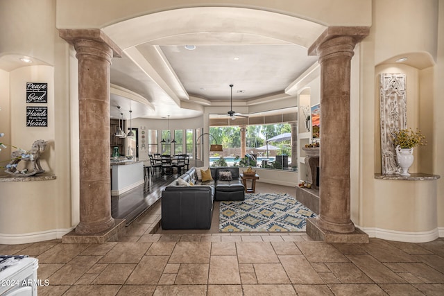 living room featuring ceiling fan, a raised ceiling, and decorative columns