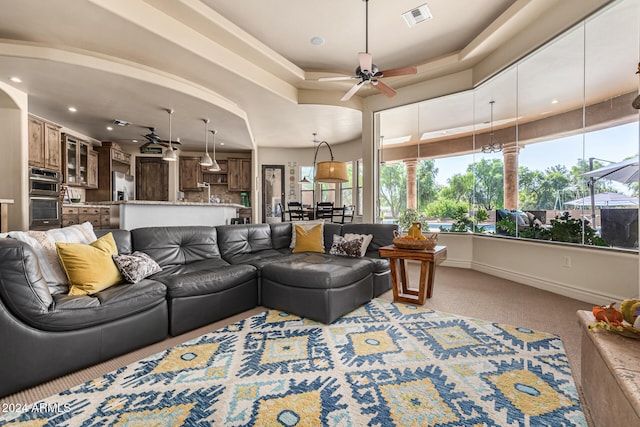 living room with a raised ceiling, ceiling fan, and light colored carpet