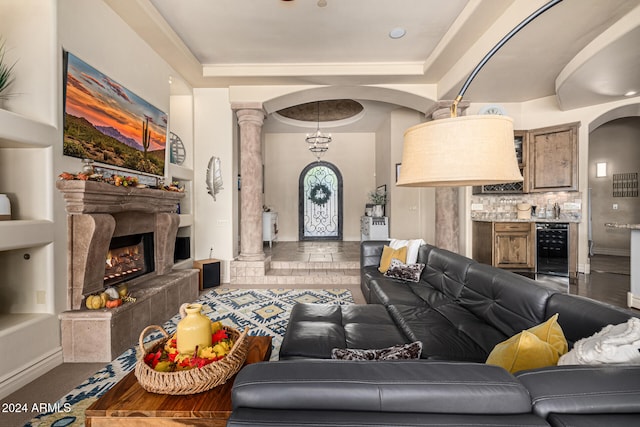 living room with a tray ceiling, ornate columns, built in shelves, and beverage cooler