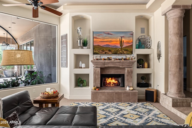 living room featuring ceiling fan, a tiled fireplace, built in features, and ornate columns