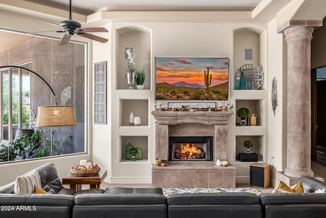 living room with decorative columns, built in shelves, ceiling fan, and a tile fireplace