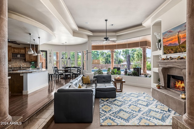 living room with ceiling fan, sink, dark wood-type flooring, a tray ceiling, and a fireplace