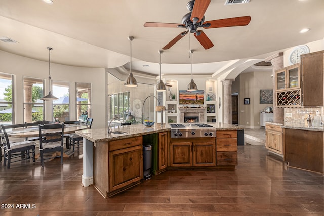 kitchen with hanging light fixtures, light stone countertops, stainless steel gas stovetop, and dark wood-type flooring