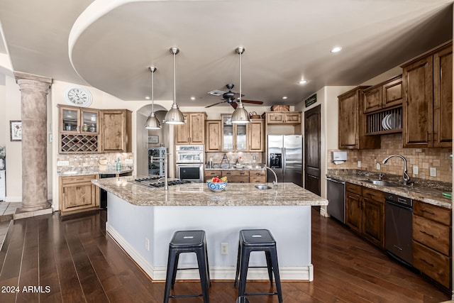 kitchen with appliances with stainless steel finishes, dark hardwood / wood-style flooring, ornate columns, sink, and an island with sink