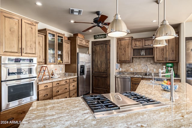 kitchen with ceiling fan, stainless steel appliances, tasteful backsplash, light stone counters, and decorative light fixtures