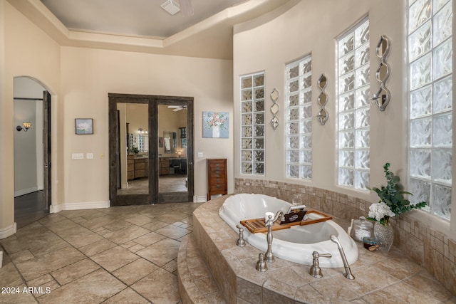 bathroom with a healthy amount of sunlight, a tray ceiling, tiled bath, and french doors