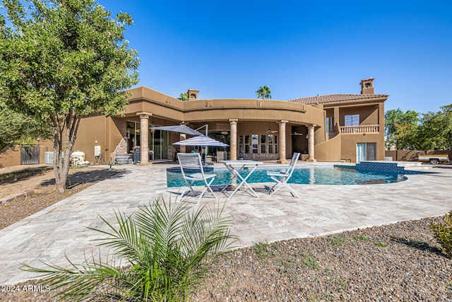 back of property featuring a swimming pool with hot tub, a patio area, and a balcony