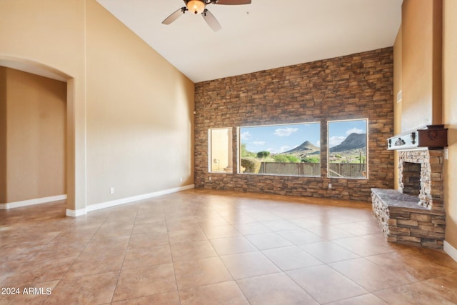 unfurnished living room featuring a stone fireplace, light tile patterned flooring, high vaulted ceiling, and ceiling fan