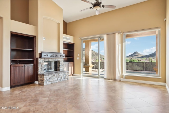 unfurnished living room featuring a fireplace, a mountain view, built in shelves, and ceiling fan