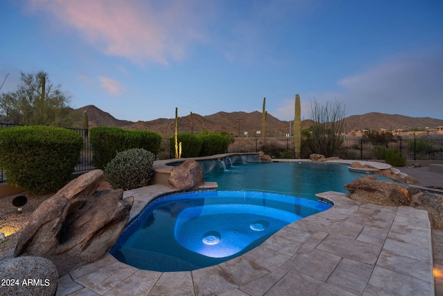 pool at dusk featuring pool water feature, a mountain view, an in ground hot tub, and a patio area