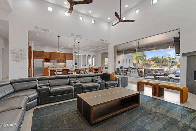 tiled living room with ceiling fan, sink, a fireplace, and a high ceiling