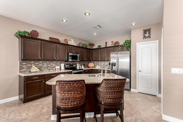 kitchen with dark brown cabinetry, sink, a center island with sink, and appliances with stainless steel finishes