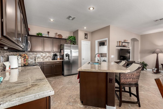 kitchen with sink, light stone counters, tasteful backsplash, a center island with sink, and appliances with stainless steel finishes